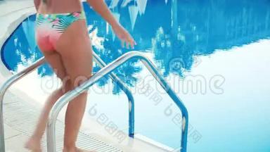 身着比基尼和太阳镜的年轻黑发女子在阳光明媚的夏日走进游泳池游泳